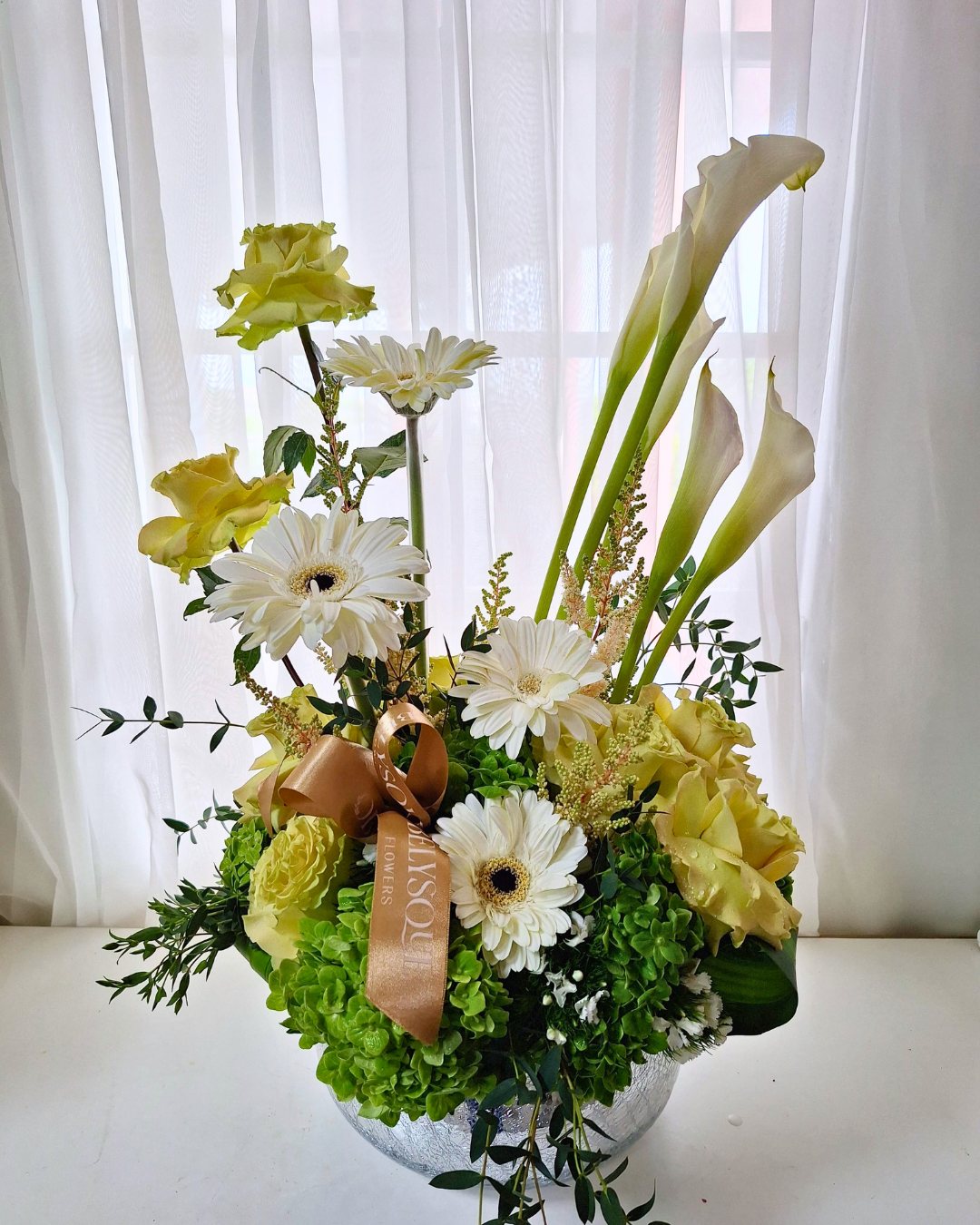 Calla lilies, gerberas and green hydrangea with a gold Obelysque ribbon